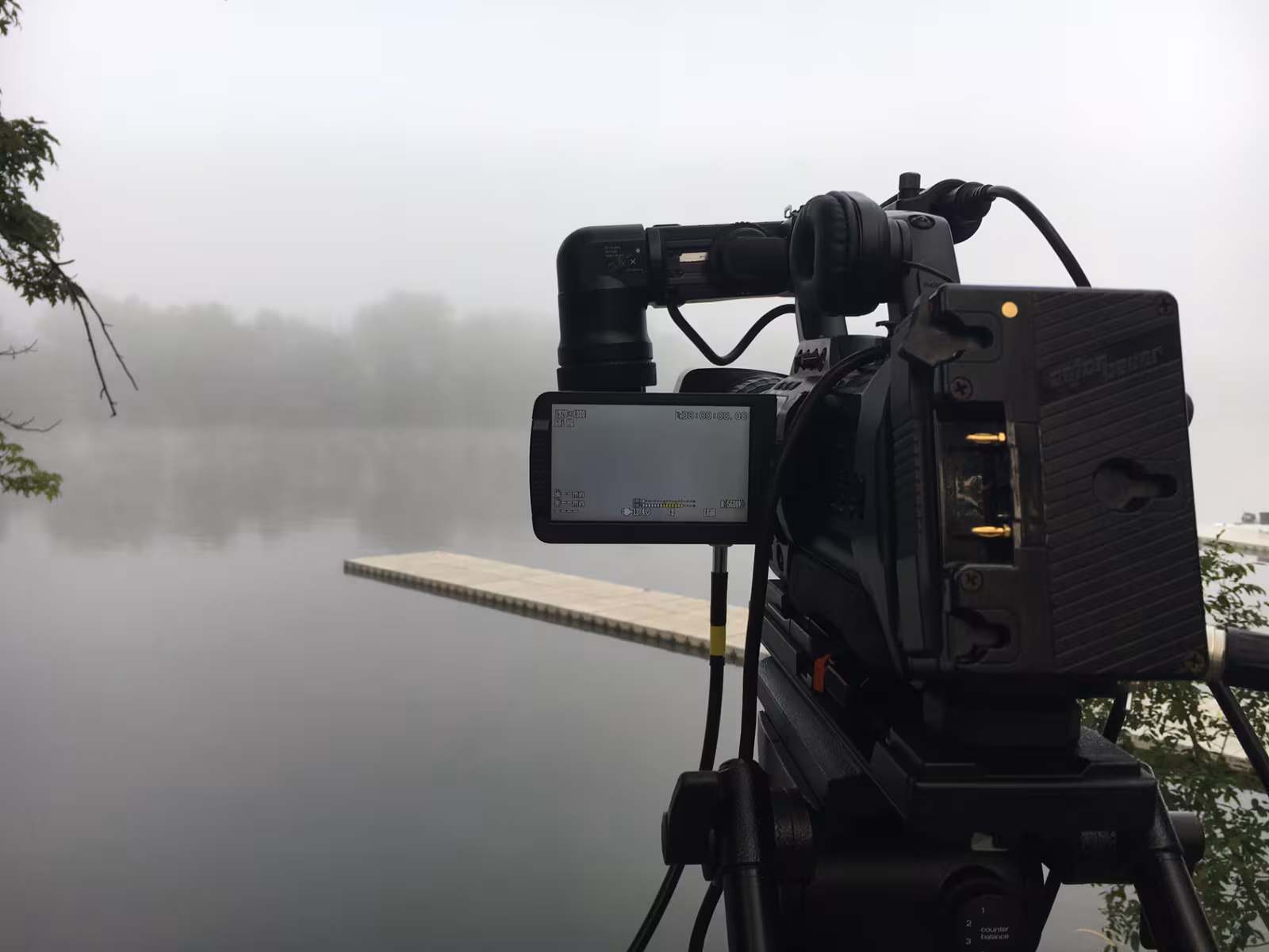 Broadcast camera framed on a dock over a fog-covered lake at sunrise
