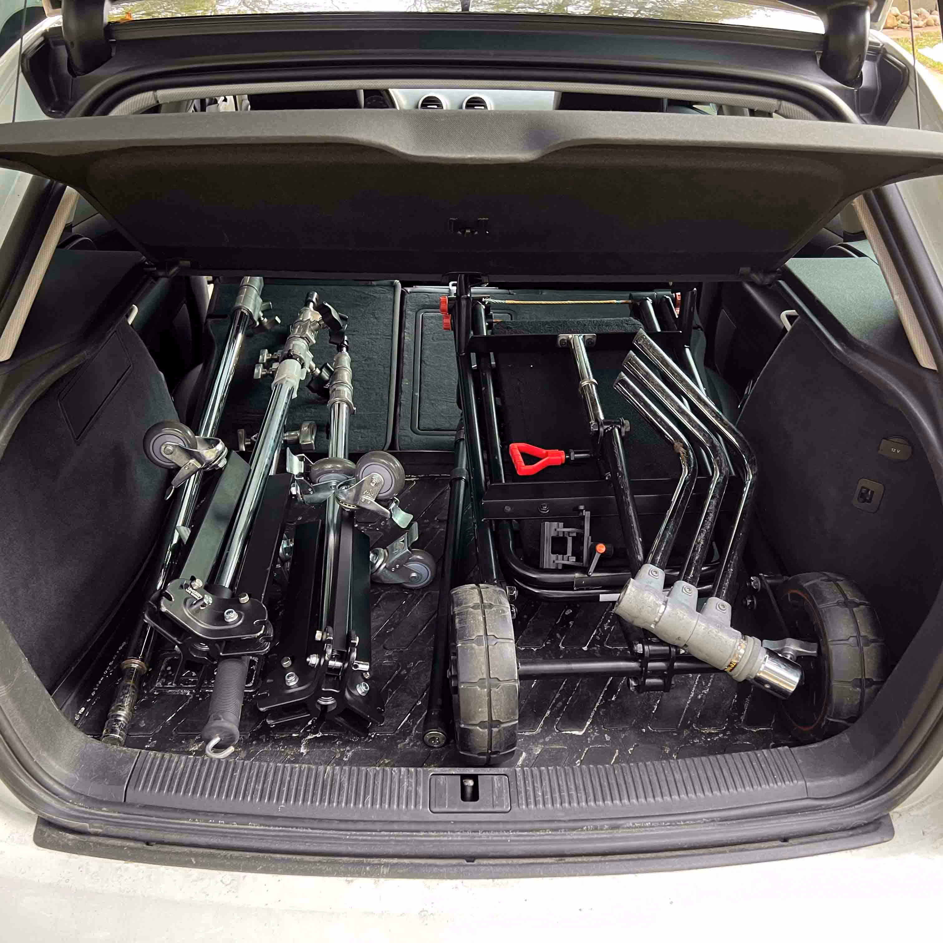Car trunk open showing folded film equipment stands and carts