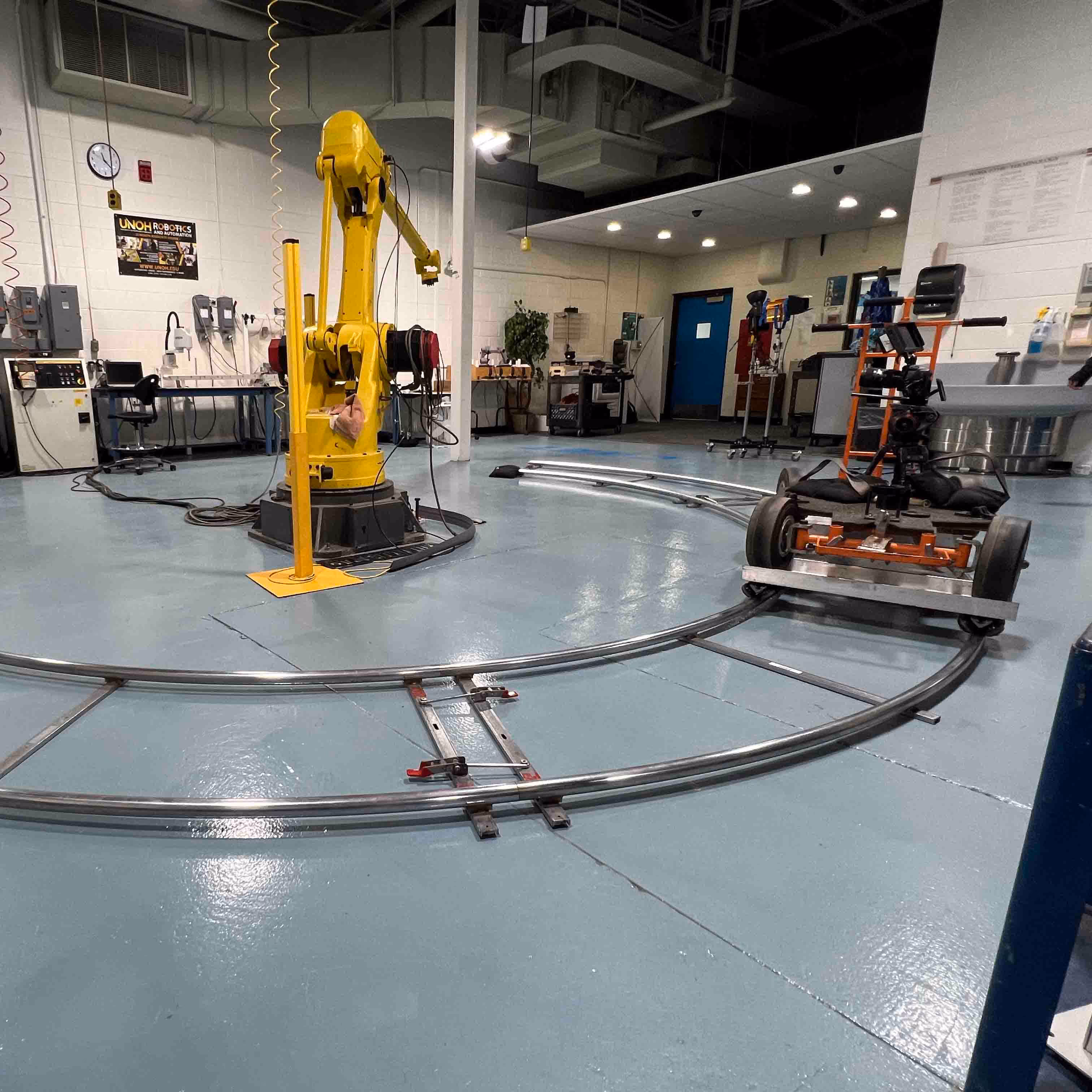 Yellow industrial robotic arm inside a workshop with a camera dolly on track
